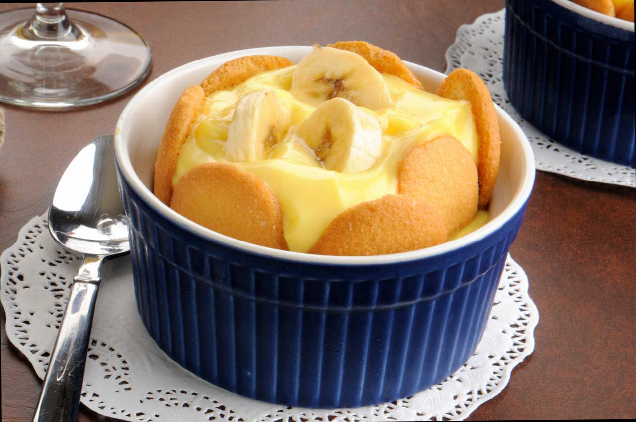 Individual serving of banana pudding topped with fresh banana slices and vanilla wafers in a blue ramekin.