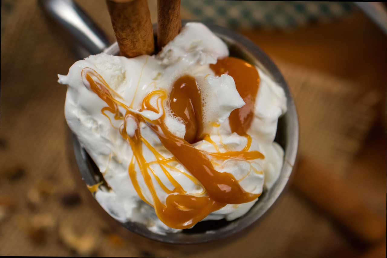 Whipped cream dessert topped with caramel drizzle and wafer sticks in a metallic cup.