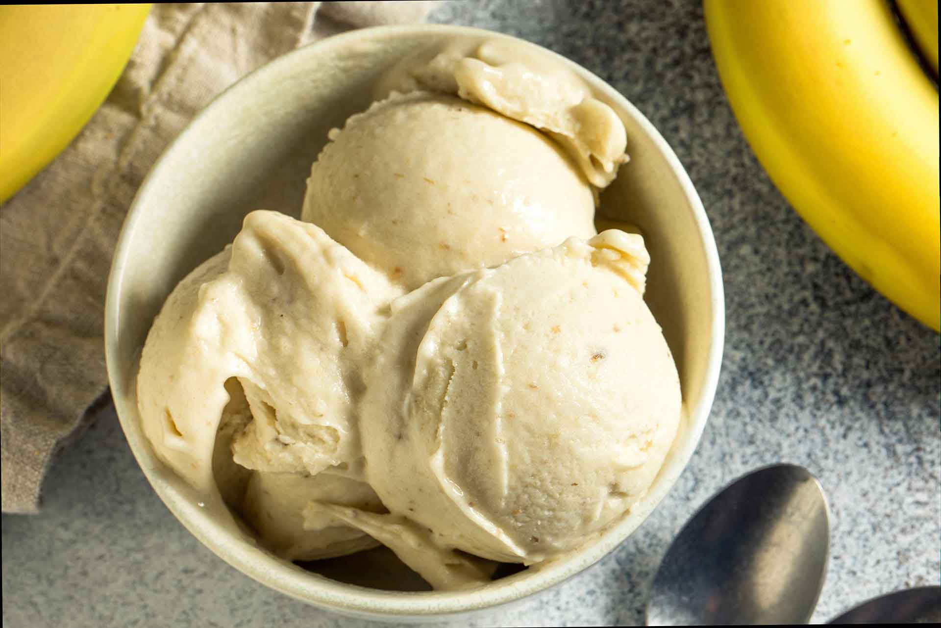 A person scooping banana ice cream into a bowl with a metal spoon.