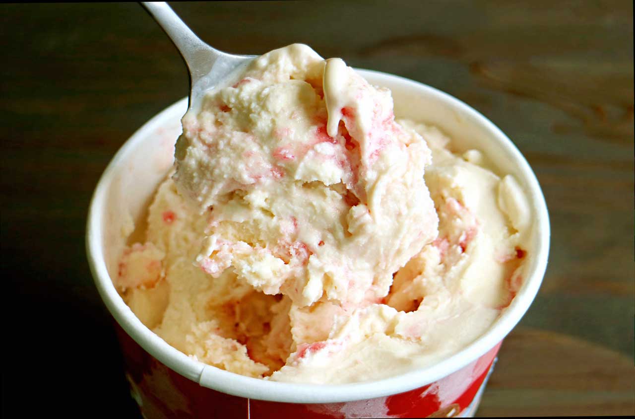 Cup of strawberry and vanilla ice cream with spoon scooping a portion.
