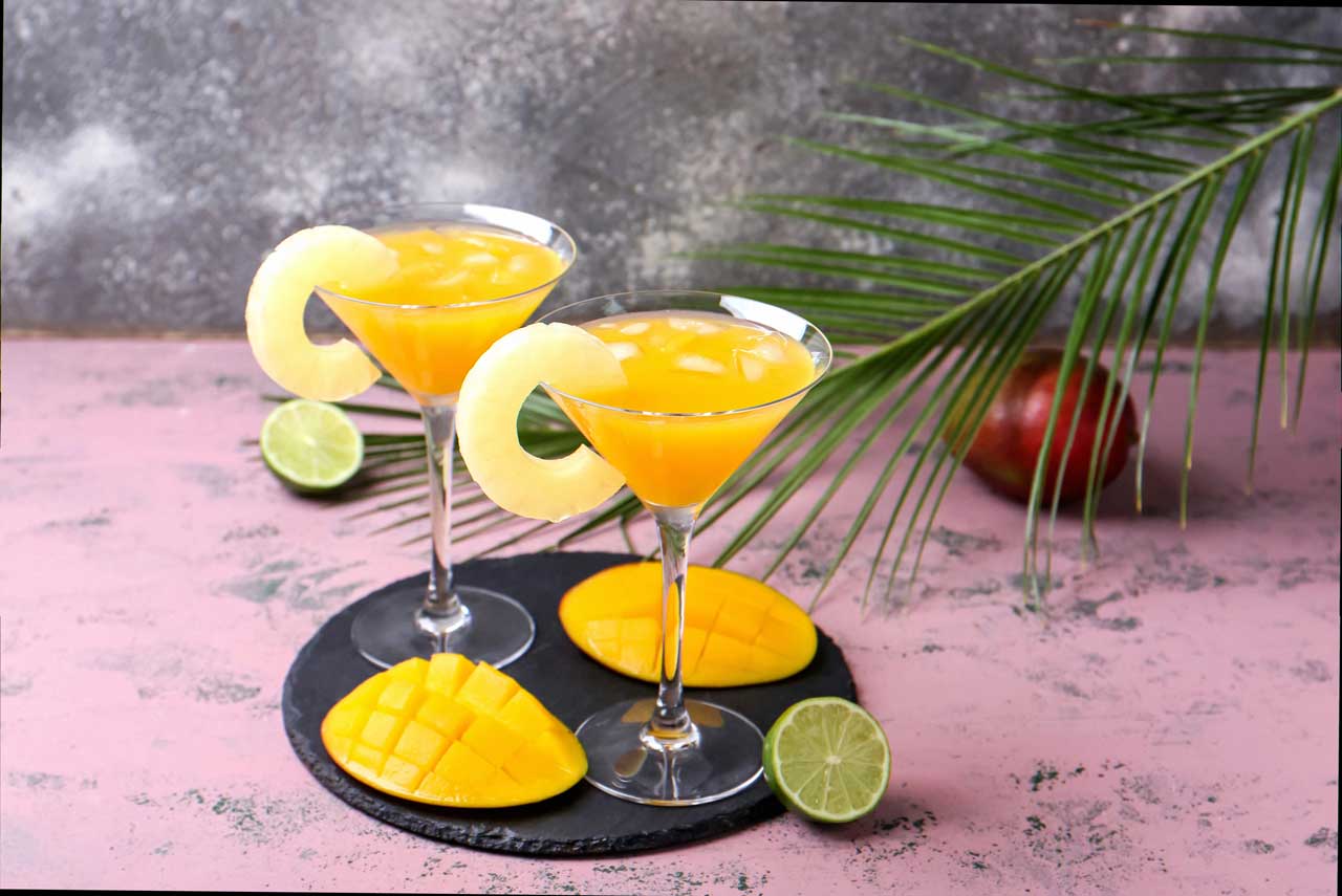 Two martini glasses filled with orange tropical cocktails garnished with pineapple slices.